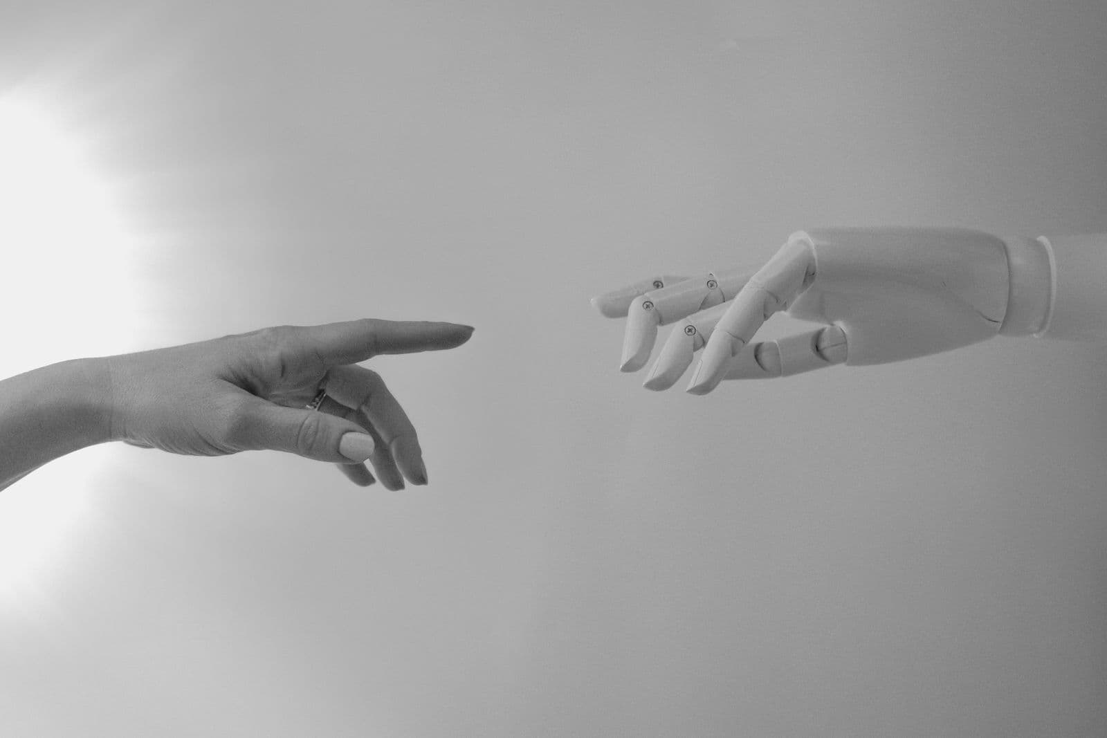 A human hand and a white robotic hand reaching toward each other, fingertips almost touching.